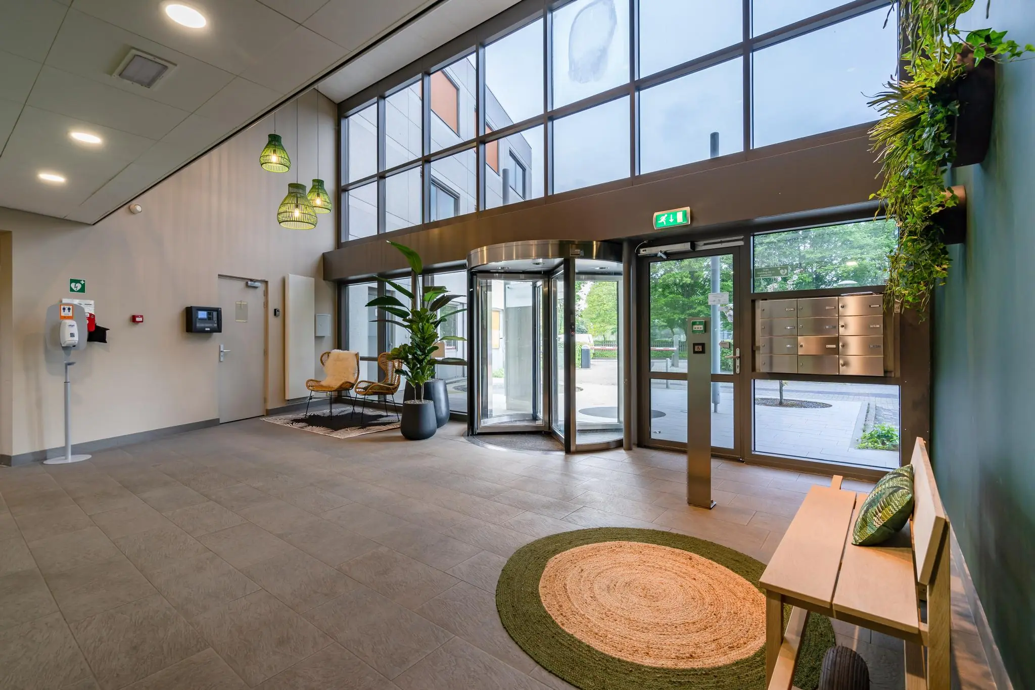 Moderne en gastvrije entreehal aan de Baarnsche Dijk met glazen draaideur, zithoek en planten.